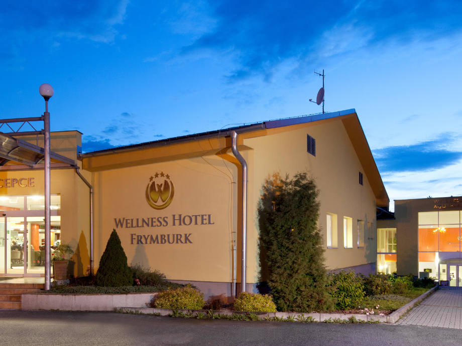 Exterior view of Wellness Hotel Frymburk at dusk with blue sky and landscaping in front of the entrance sign.