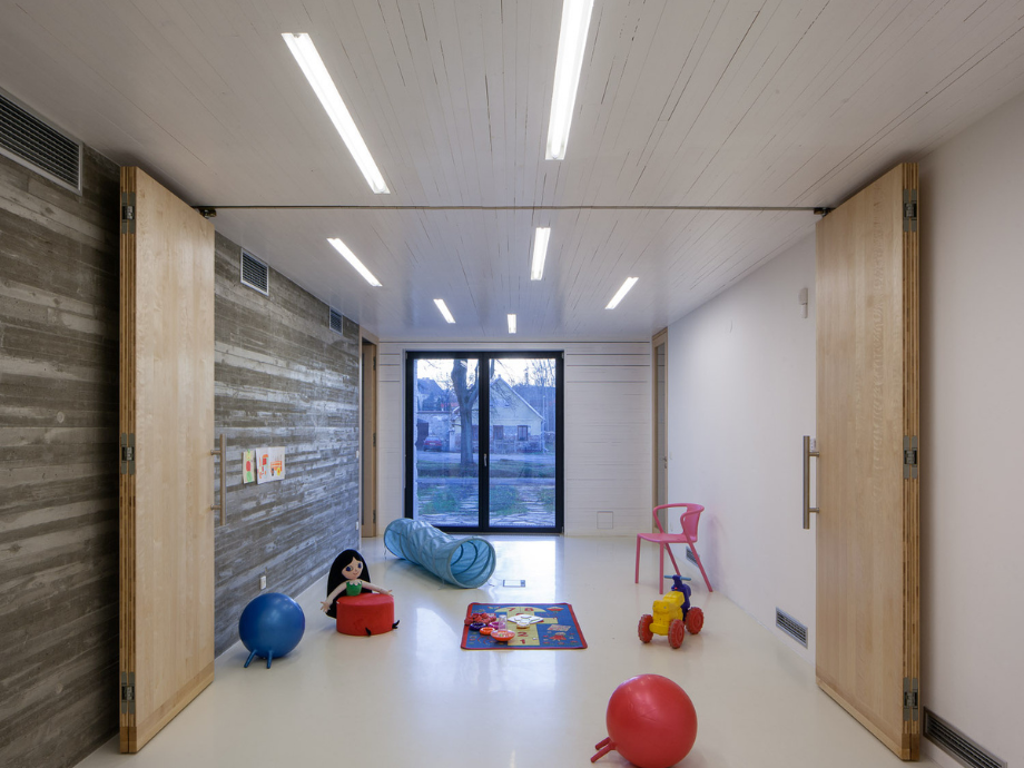 Playroom with large window at end, white floor, and toy vehicles, ball, and rug scattered around.