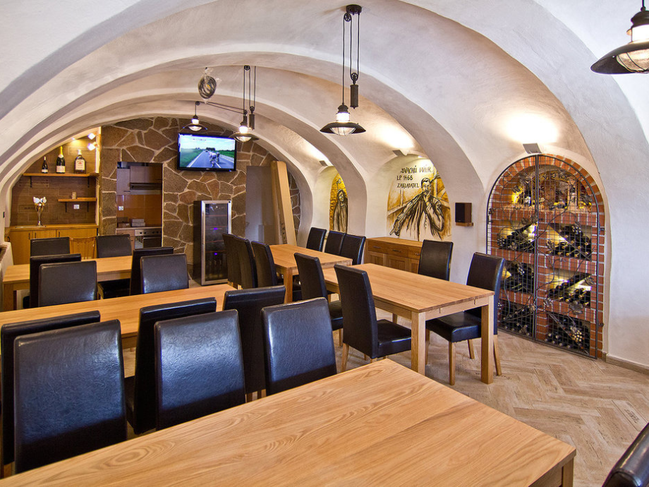 Restaurant dining room with arched white ceilings, wooden tables, black chairs, and a wine rack along the wall.