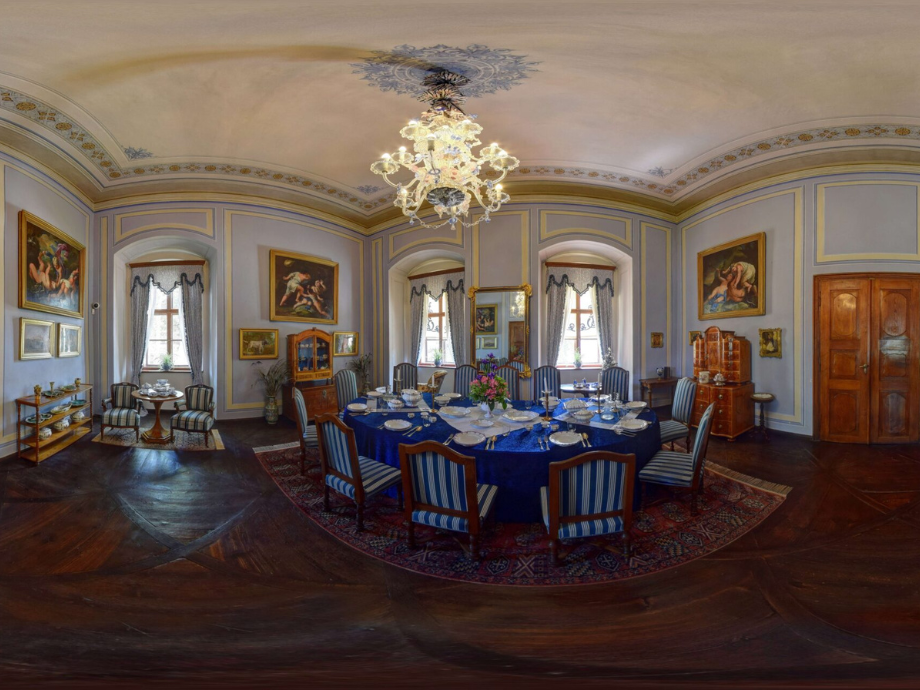 Round table set for a formal banquet in an elegant blue-draped dining room with a crystal chandelier above.