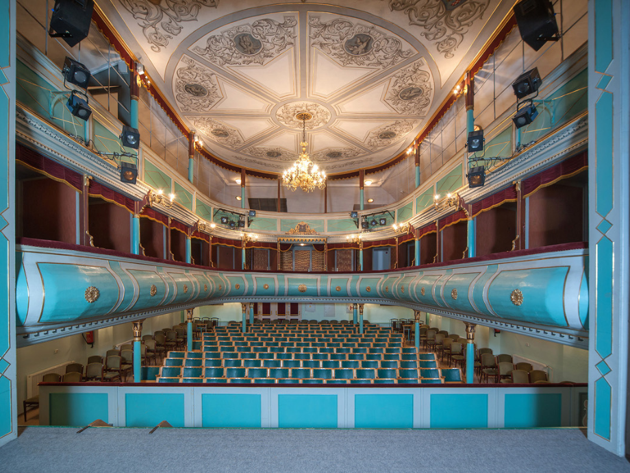 Historic opera house interior with turquoise balconies, gold accents, and a crystal chandelier overhead