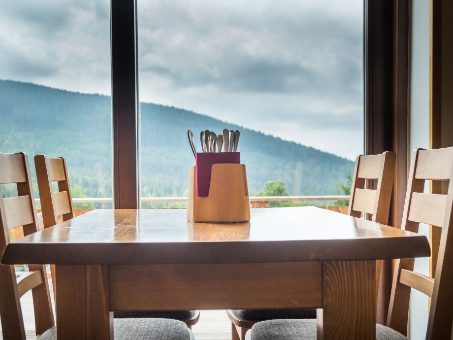 Wooden dining table with a utensil caddy, set beside large windows overlooking mountains.