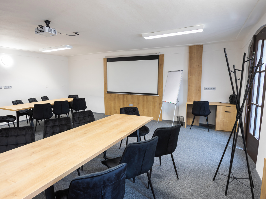 Conference room set up for a presentation with long wooden tables, black upholstered chairs, and a large screen at the front.