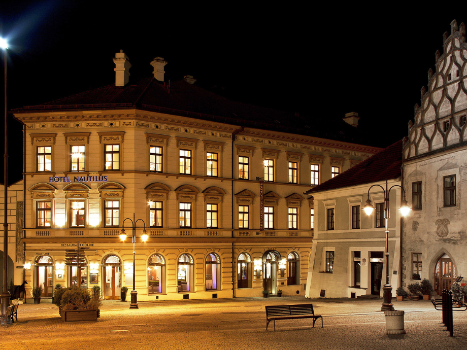 Night view of Hotel Nautilus, a historic, lit building with arched ground-floor windows in a cobblestone square.