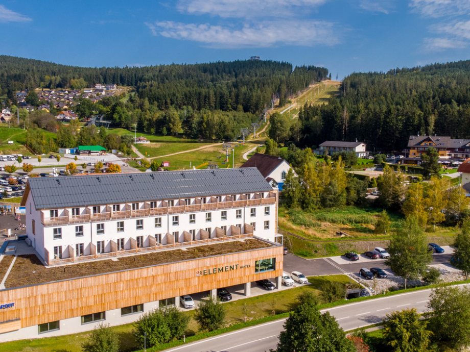 A white hotel with a brown facade labeled 'ELEMENT Hotel' beside a road, with hills and a ski slope in the background.