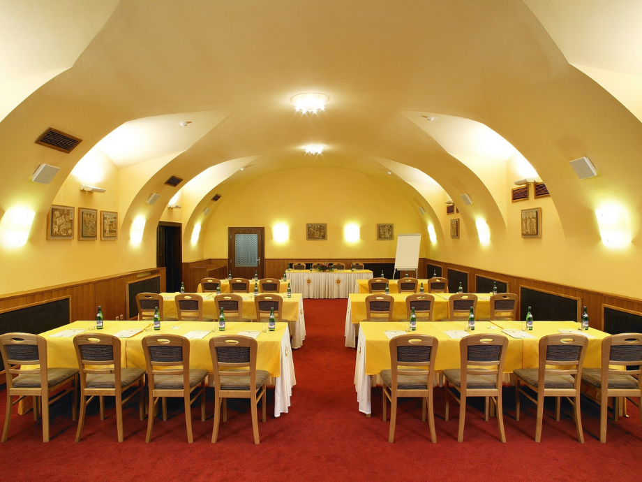 Conference room with arched ceiling, yellow walls, red carpet, and rows of tables set with yellow tablecloths and bottled water for a meeting or training.