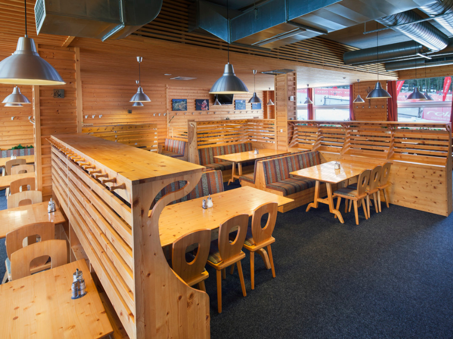Warm wood-paneled dining area with booths, wooden tables, and striped cushioned seating in a casual restaurant interior, with metal pendant lights and exposed ducts on the ceiling.
