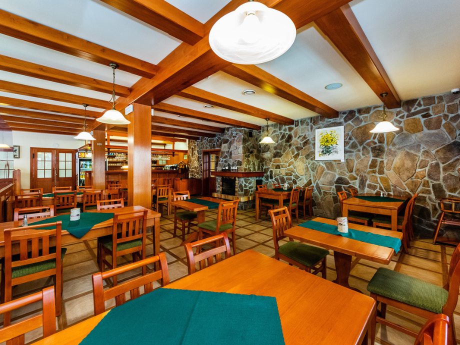 Cozy restaurant dining area with wooden tables and green chairs, teal table runners, and a stone wall with a fireplace.