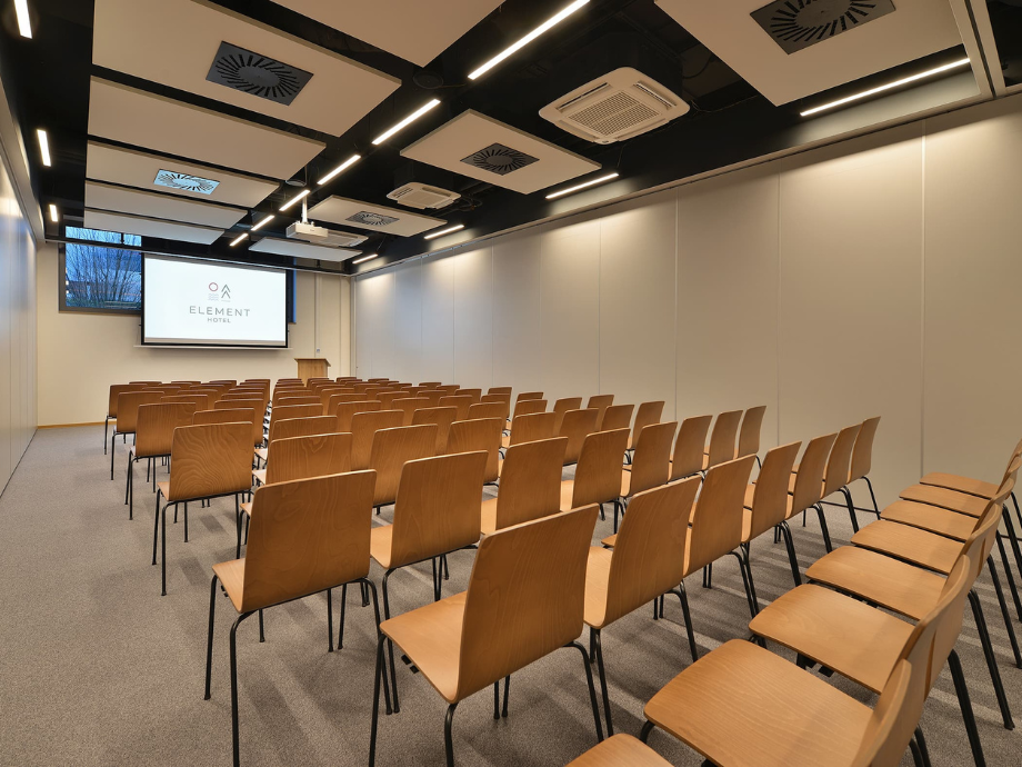 Lecture room with rows of wooden chairs facing a projection screen displaying the Element Hotel logo.