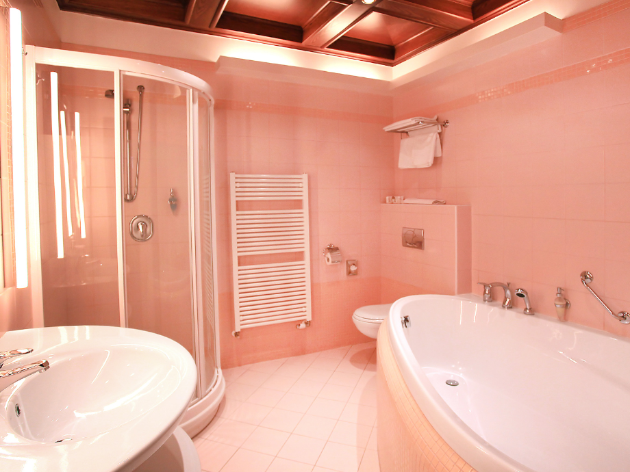 Pink-tiled bathroom with a curved glass shower, a white freestanding tub, sink, and heated towel rail.