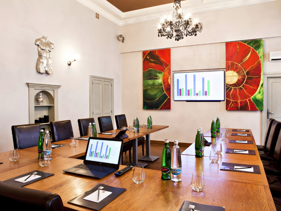 Conference room setup for a business meeting with a long wooden table, laptops showing charts, water bottles, and glasses ready for a presentation.