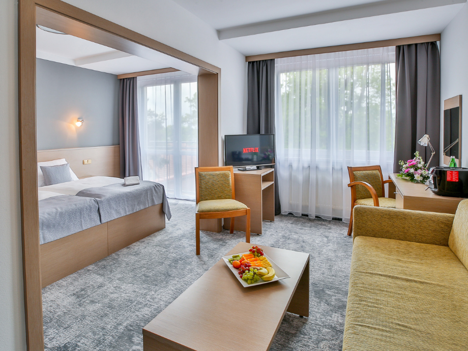Hotel suite: two single beds, a seating area, and a fruit platter on the coffee table.