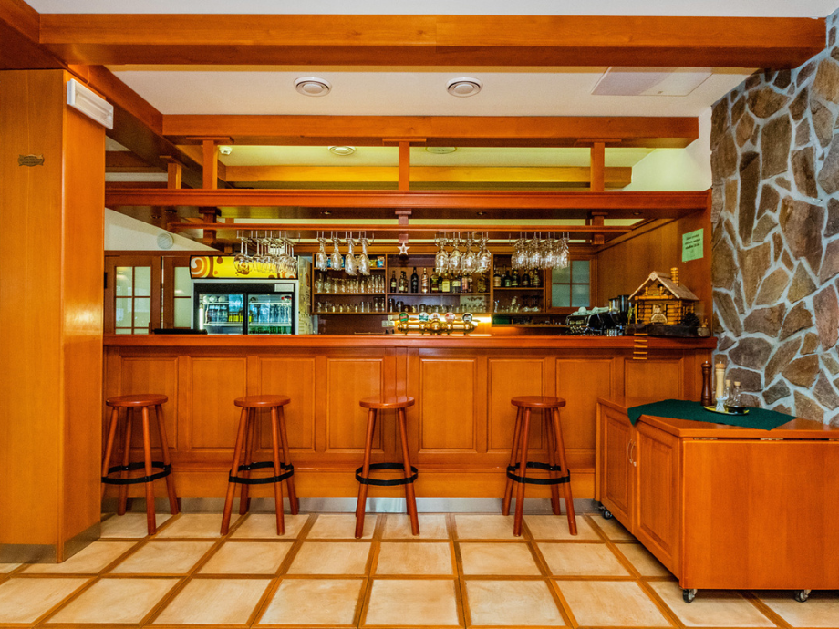 Cozy wooden bar with four stools, hanging wine glasses, and a stone wall on the right.