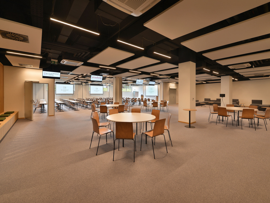 Large conference room set up with round tables and tan chairs, projector screens along the back wall.