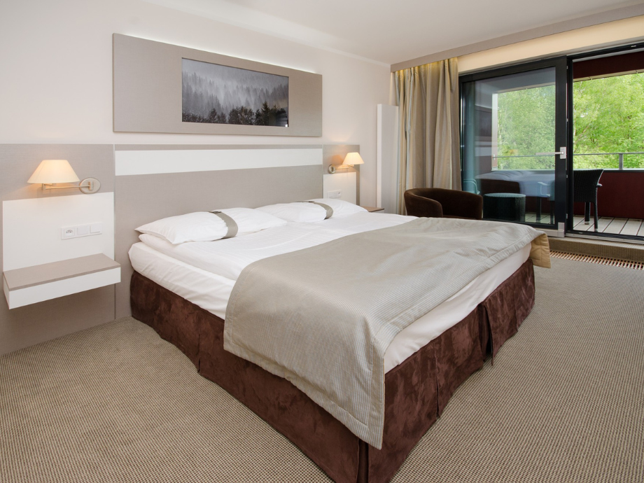 Hotel room with a large bed, neutral tones, and a balcony view through glass doors.