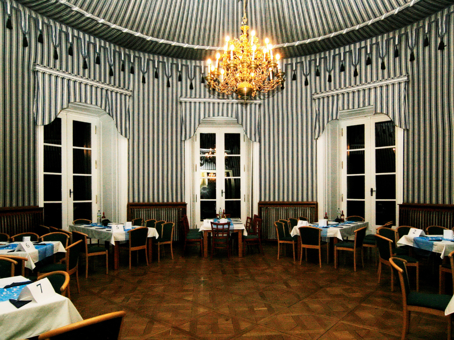 Banquet dining room with blue-and-white striped wallpaper, a gold chandelier, and tables set with white cloths.