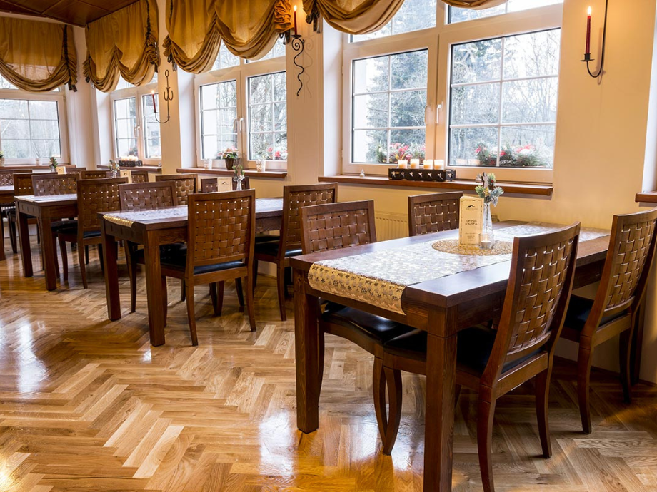 Warm dining room with dark wood tables and woven chairs, large windows, and candle sconces in a sunlit setting.