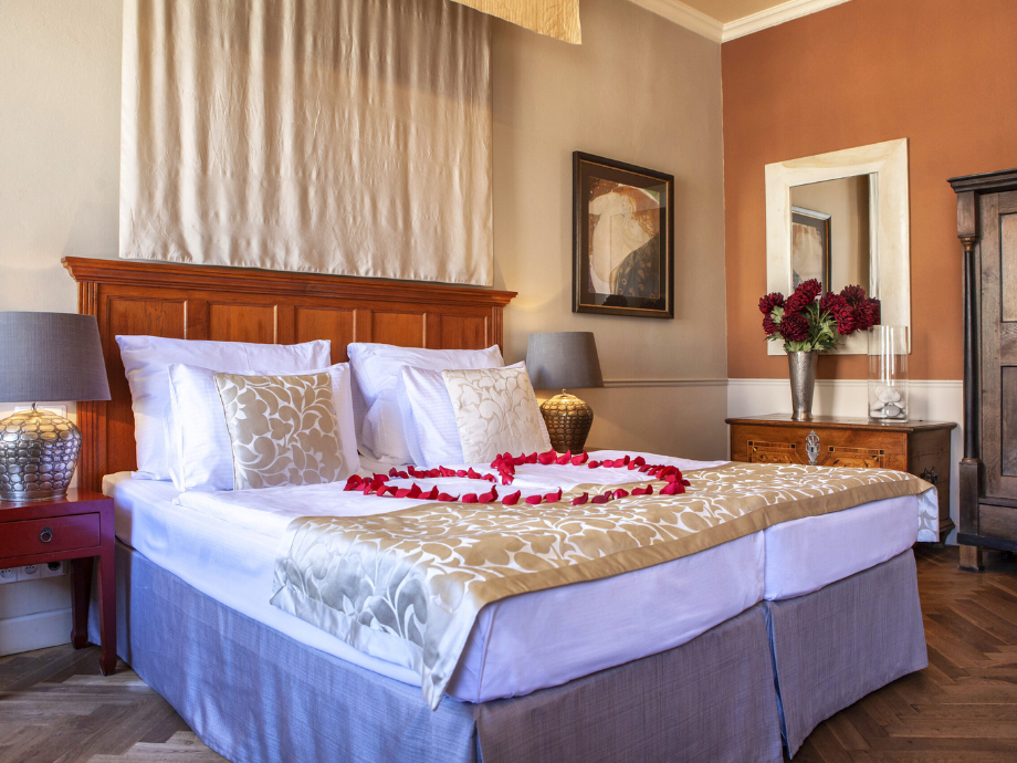 Romantic hotel bedroom with two twin beds pushed together, rose-petal heart centerpiece, and warm lighting and decor.