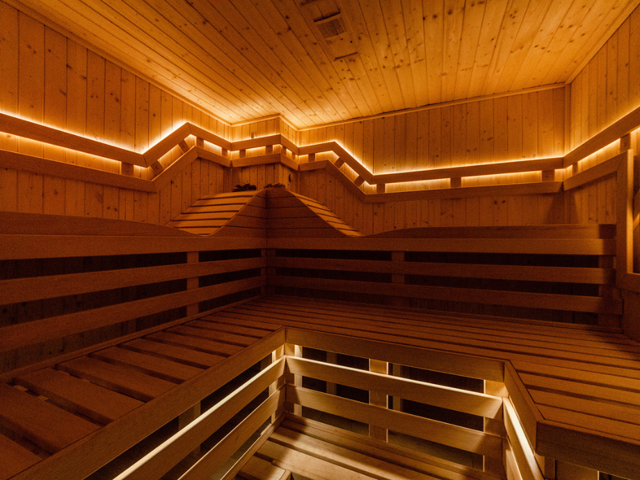 Interior of a wooden sauna with tiered benches and warm orange lighting along the walls and ceiling.