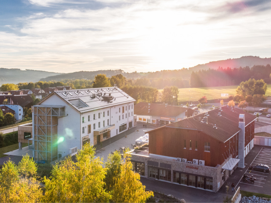 Aerial view of a small town bathed in warm sunset light, showing white and red buildings, trees, and surrounding hills.