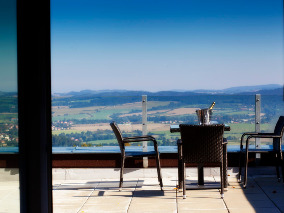 Balcony seating with two wicker chairs and a table on a terrace overlooking a rural valley and hills in the distance, a champagne bucket on the table.