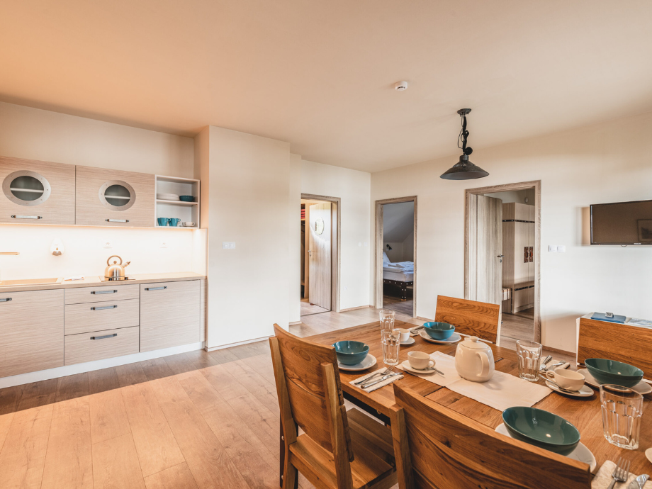 Open kitchen and dining area with a wooden table set for breakfast, teal bowls, cups, and a teapot on the table.