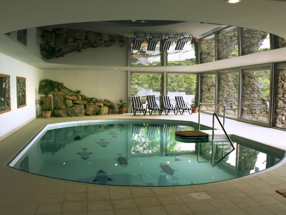 Indoor pool with turquoise water, tiled deck, and striped lounge chairs by large glass windows.
