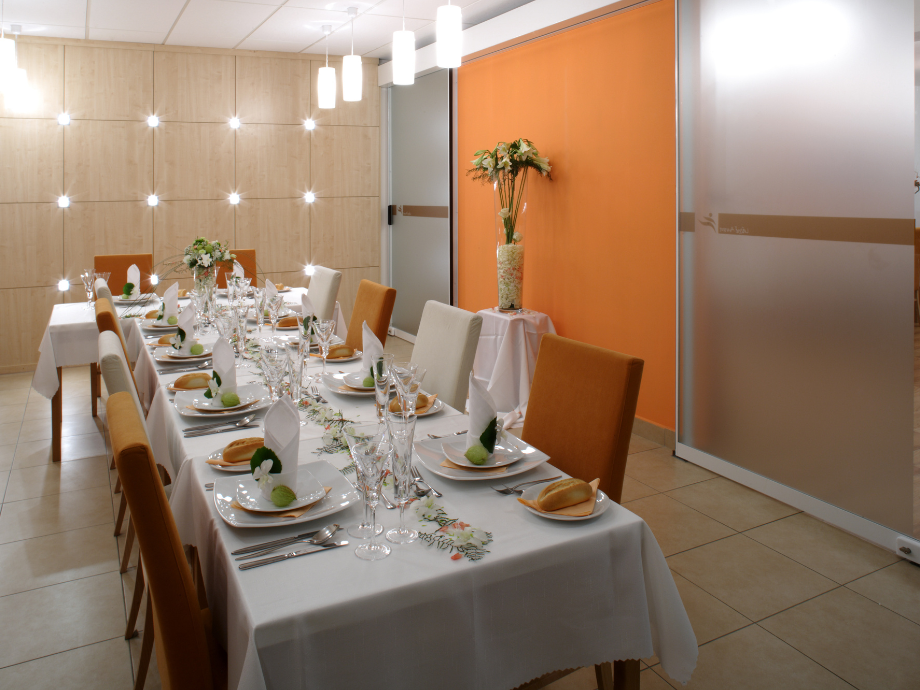 Banquet table set for a formal meal with white tablecloths, folded napkins, glassware, and floral centerpieces in a modern dining room.