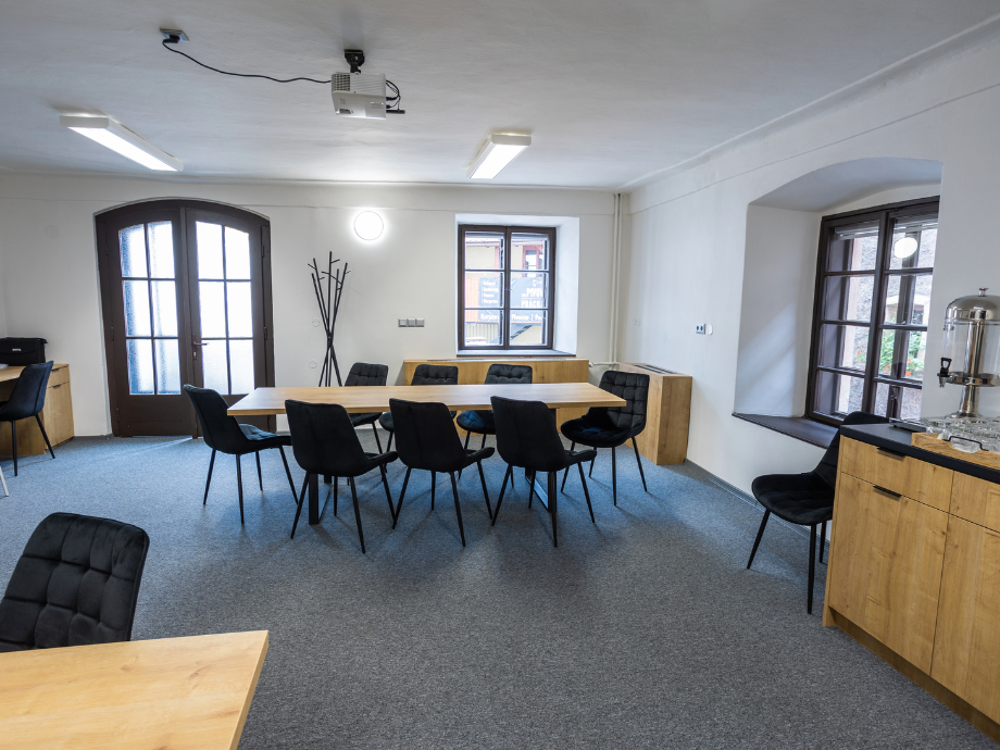 Meeting room with a long wooden table surrounded by black chairs; coat rack and cabinets along the walls.