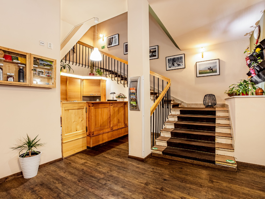 Lobby reception area with wooden desk, staircase, and framed photos hanging on the wall