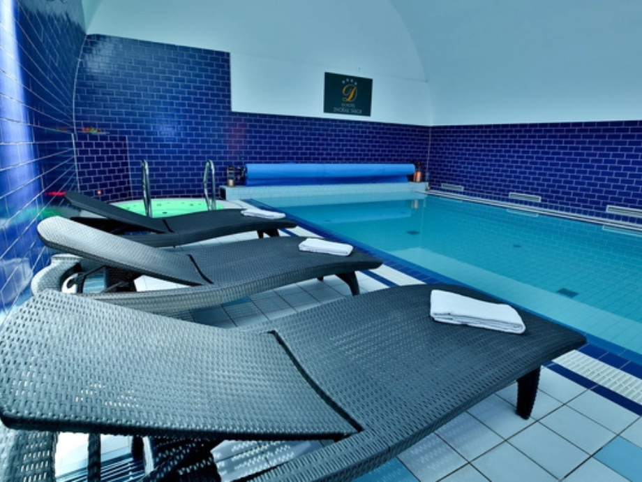 Indoor pool area with dark blue tiled walls and four black wicker lounge chairs with white towels. exploratory view of the pool deck.