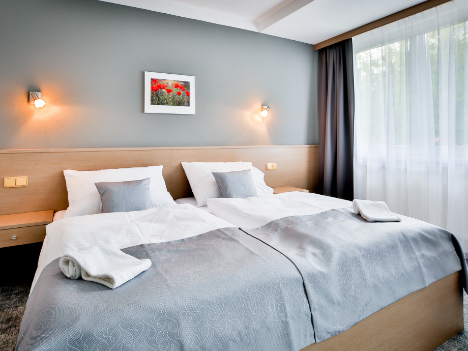 Twin beds in a modern hotel room with a gray wall, wooden headboard, and framed flower print between two wall lamps.