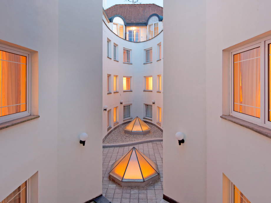 Courtyard of a white building with warm orange-lit windows and two glass pyramid skylights.