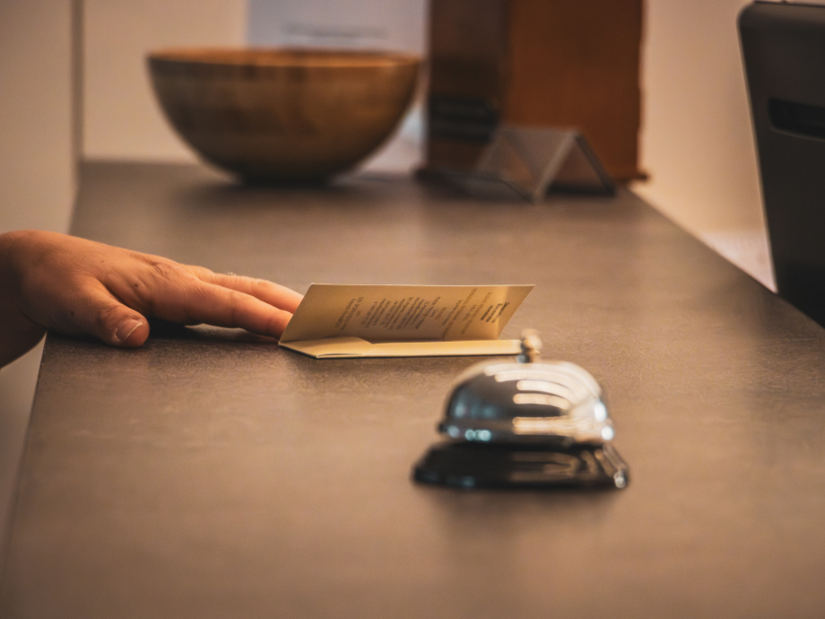 Person's hand resting on a counter with a folded card, a hotel reception bell in the foreground.