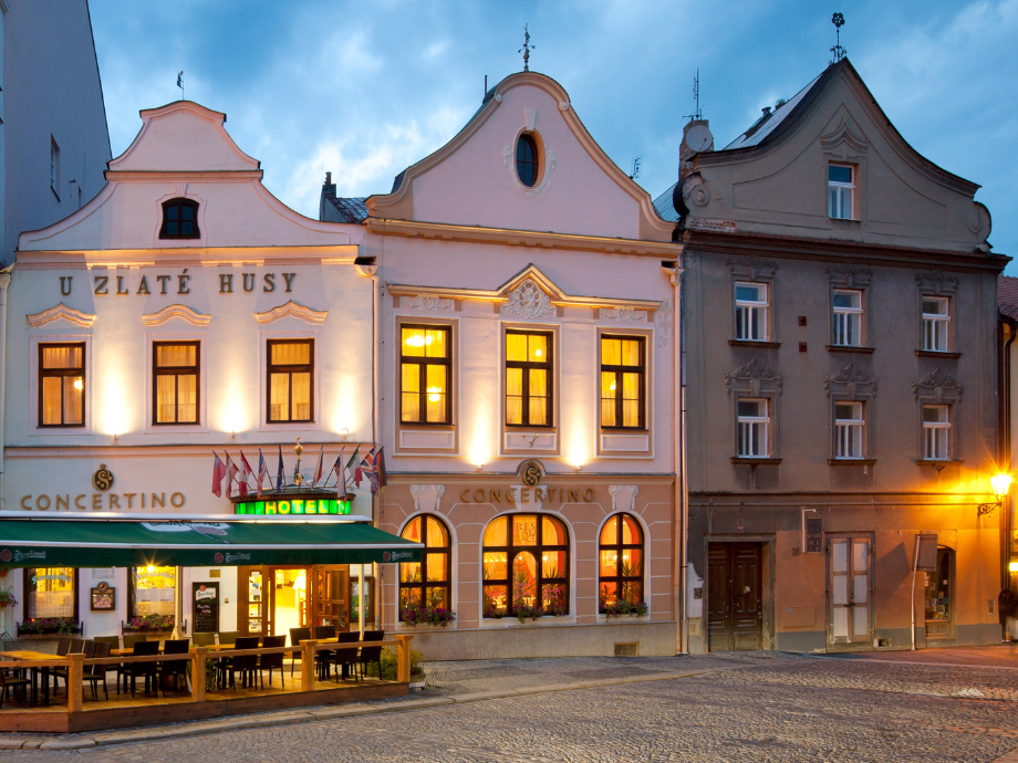Three historic townhouses at dusk with warm interior lights, and an outdoor café on a cobblestone street in front of the buildings.