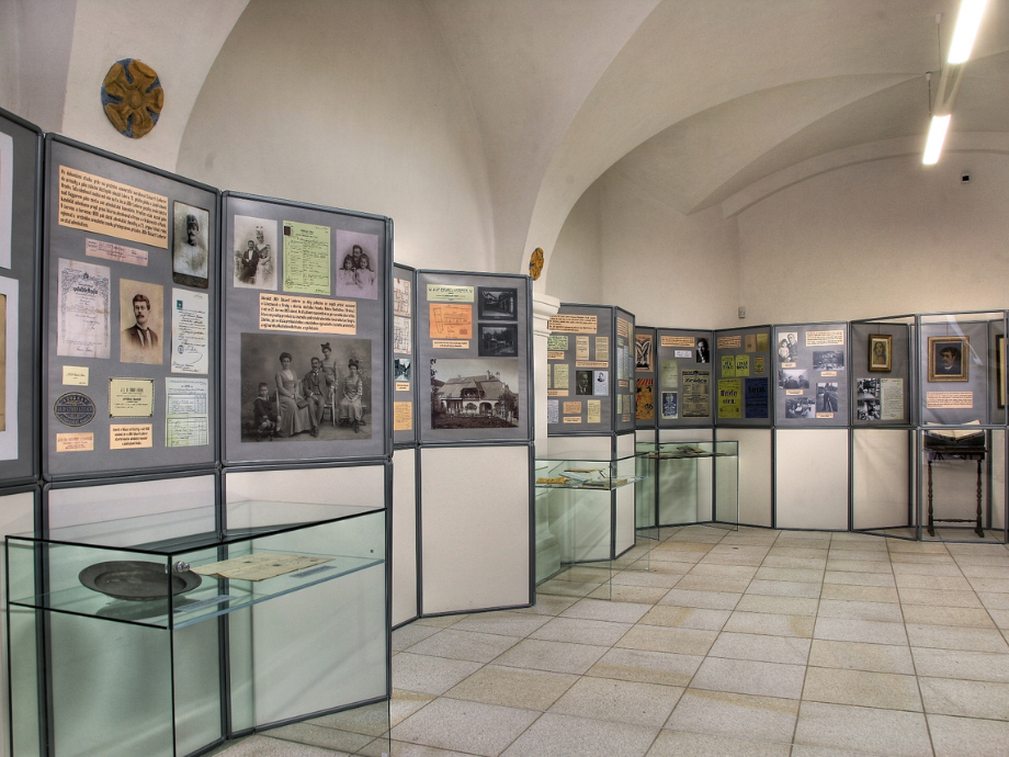 Museum exhibit with rows of display panels and glass cases containing historical photos and documents in a vaulted room.