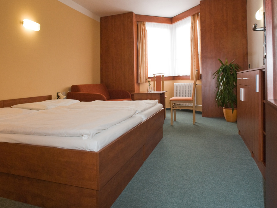 Hotel room with a wooden bed, white linens, a small seating area, and a window by the corner.