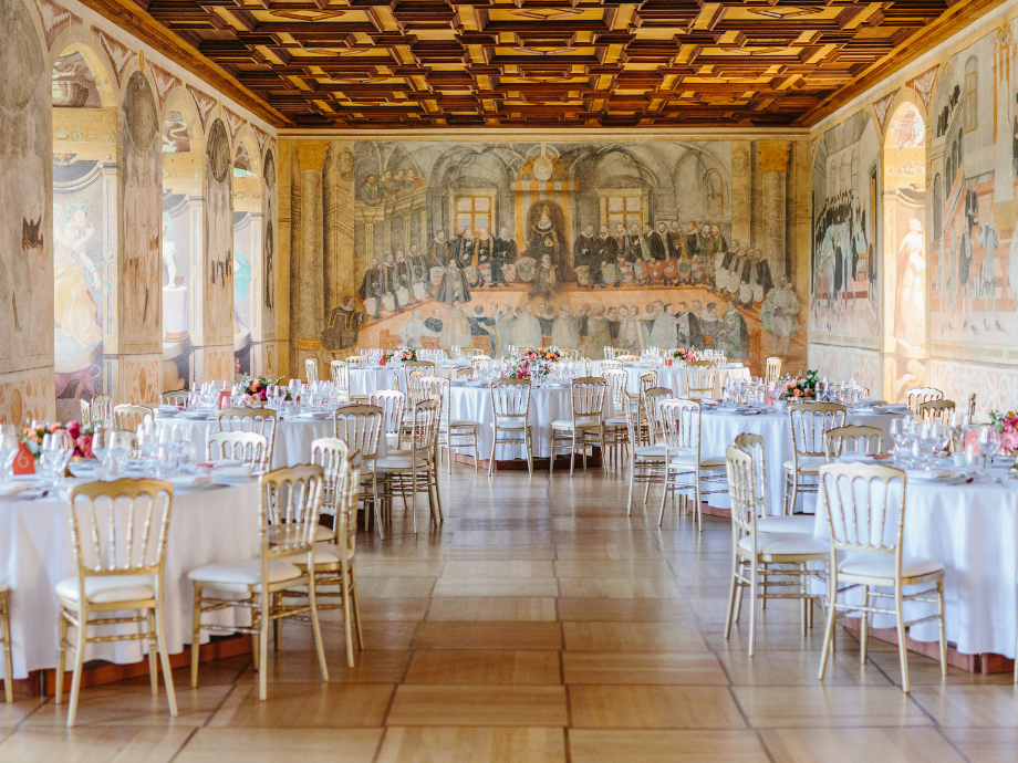 Elegant banquet hall with round tables set for a formal dinner, gold chairs, and mural-covered walls.