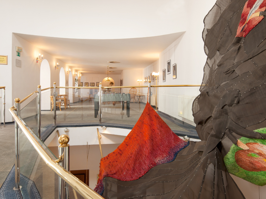 Bright art gallery with glass railings, arched doorways, and a large colorful sculpture in the foreground.