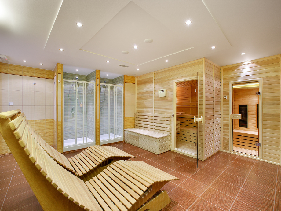 Spa room with curved wooden loungers, tiled floor, glass showers, and a wooden sauna area.