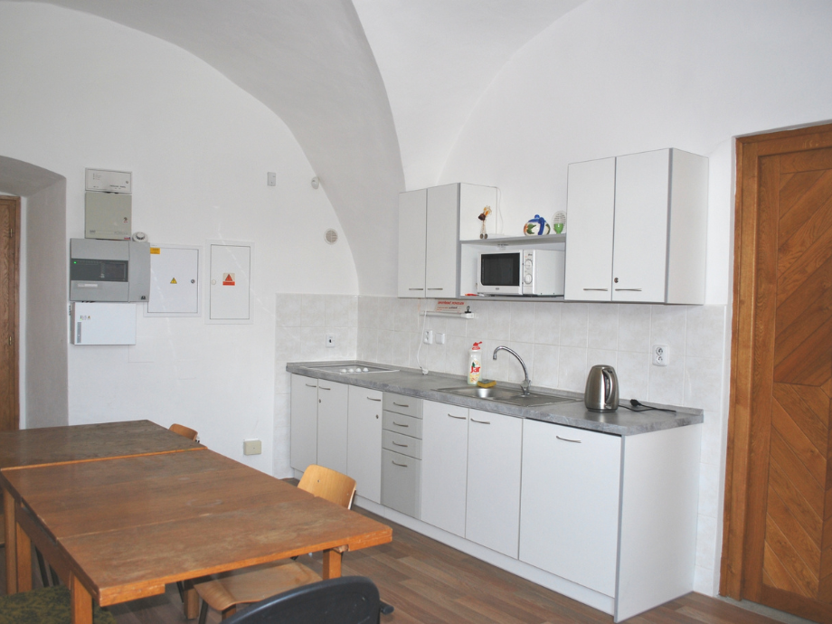White kitchen with marble countertop, upper cabinets, microwave, sink, kettle, and a wooden dining table.
