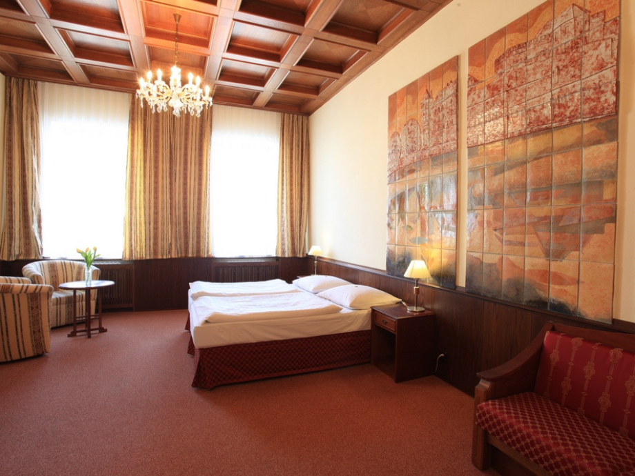 Hotel room with two beds, wood-paneled walls, and a large wall mural, plus a seating area by a round table with flowers.