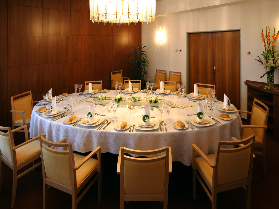 Round banquet table set for a formal dinner in a wood-paneled room, with a white tablecloth, folded napkins, plates, glasses, and beige chairs.