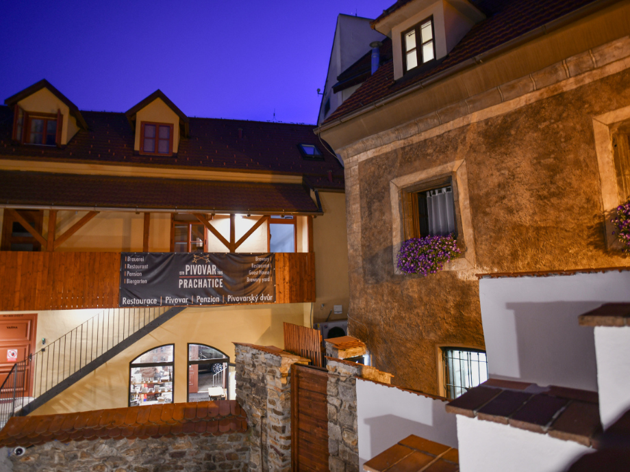 Night view of a stone-and-wood building complex with warm lights and a brewery sign at dusk.