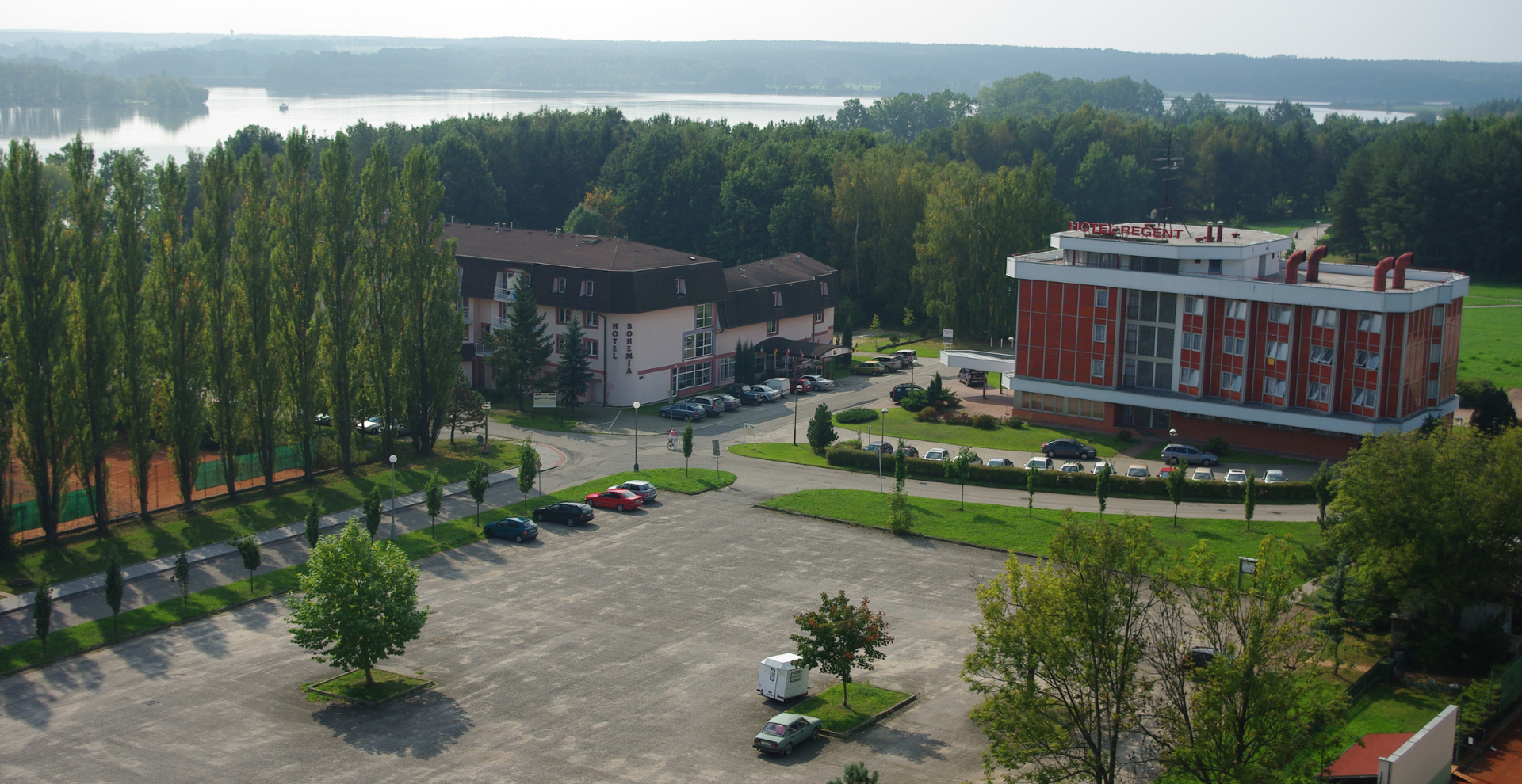 Aerial view of Hotel Regent complex with red-and-white facade, adjacent parking, and river in the distance.