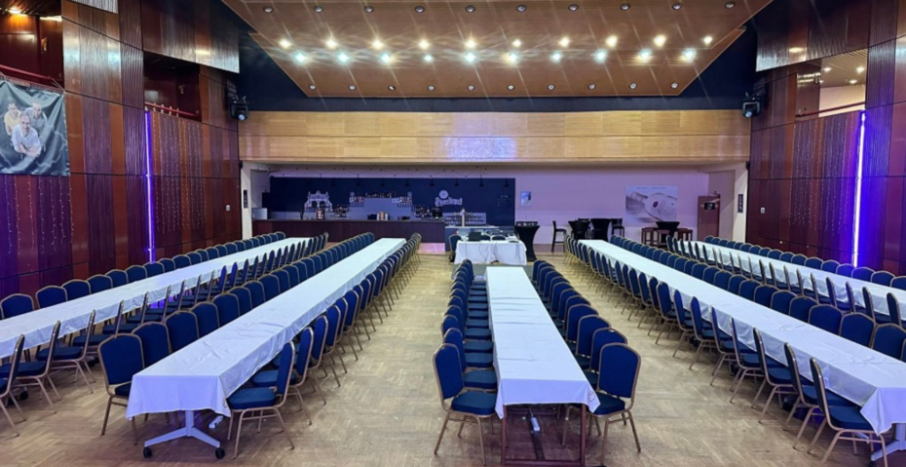 Banquet hall with long white-clothed tables and blue chairs arranged in rows for a conference.