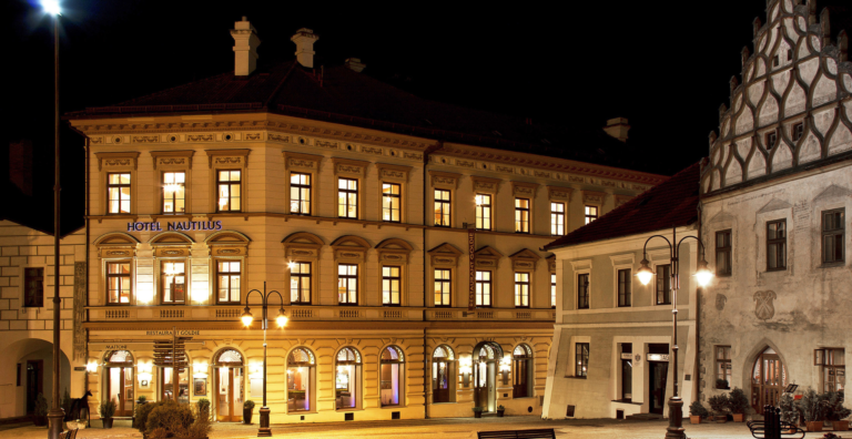 Night view of a lit historic building: Hotel Nautilus with warm interior lights and street lamps along a cobblestone square