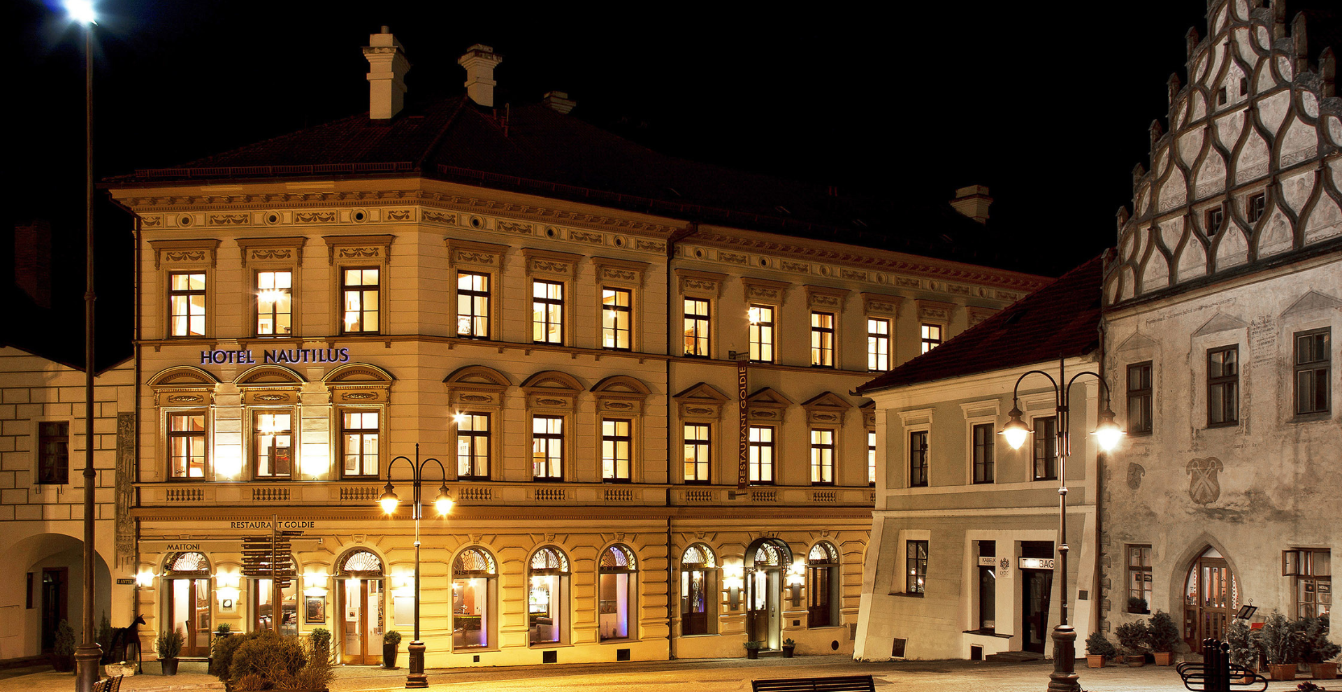 Night view of a lit historic building: Hotel Nautilus with warm interior lights and street lamps along a cobblestone square