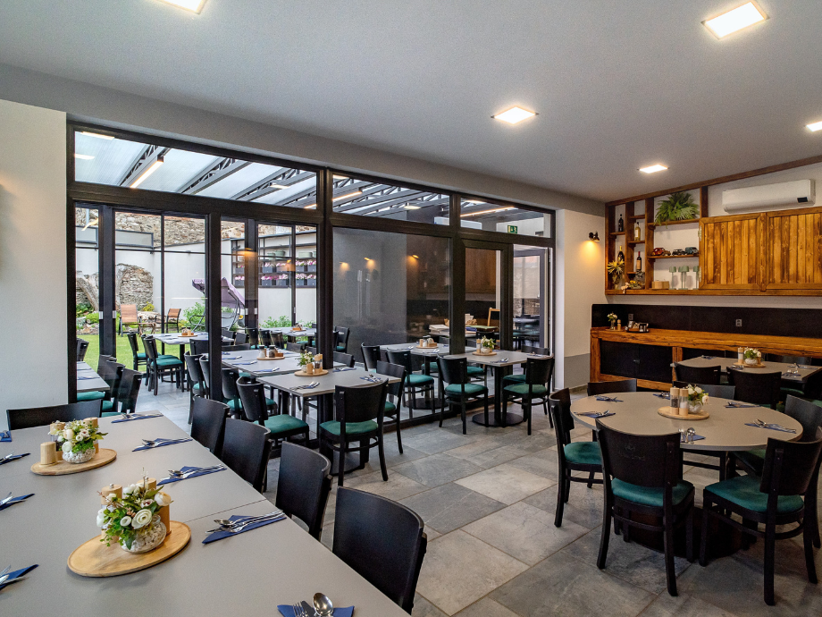 Restaurant dining area with multiple tables set with utensils and small floral centerpieces, adjacent to a glass-walled patio.