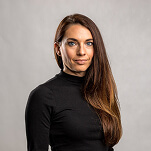 Professional headshot of a woman with long brown hair wearing a black turtleneck against a gray background.